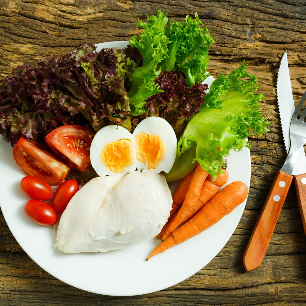 A plate of food suited for clean eating, including chicken, eggs, tomato, carrot and lettuce