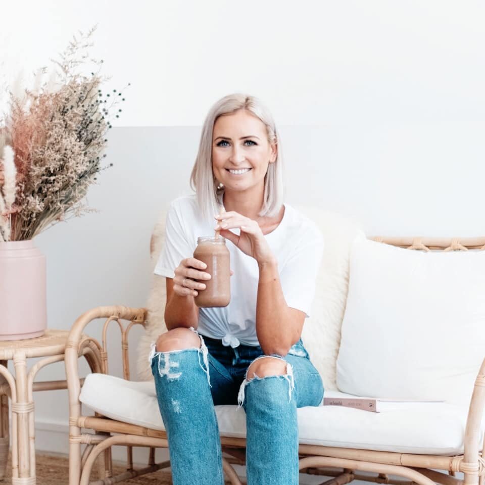 Kira Love smiling on a sofa while drinking a smoothie. She is this episode's podcast guest