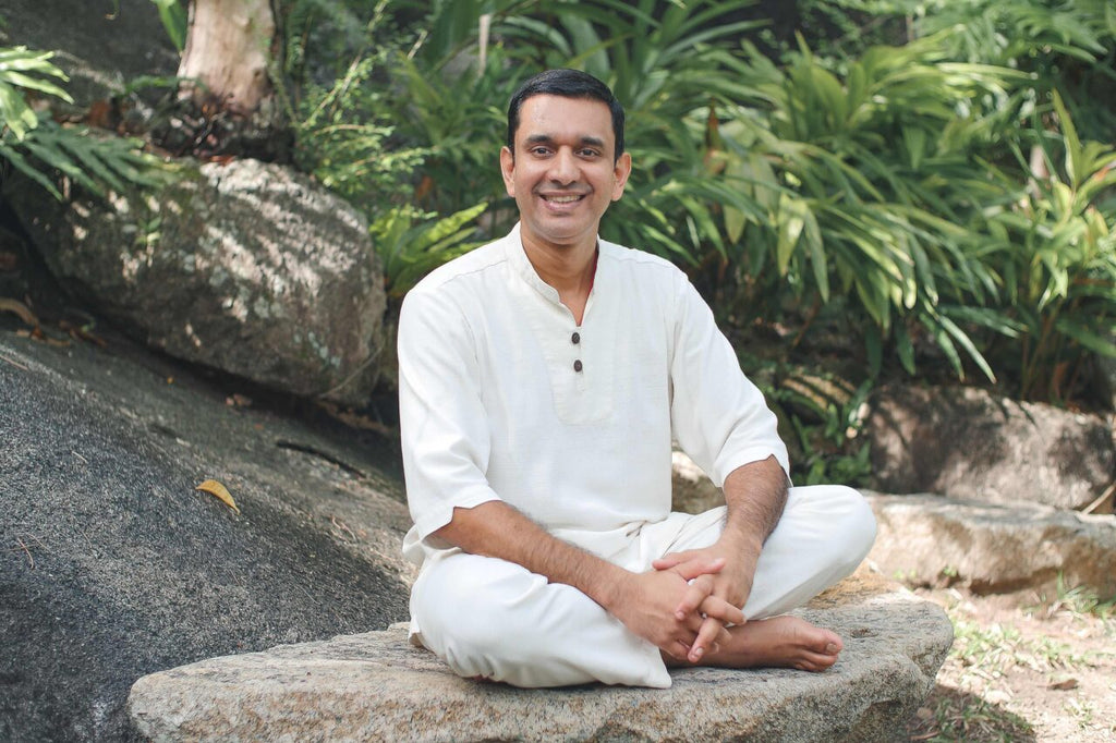 Srinivas Bhat (Kamalaya Koh Samui) sitting on a rock, taking place in morning yoga with a smile